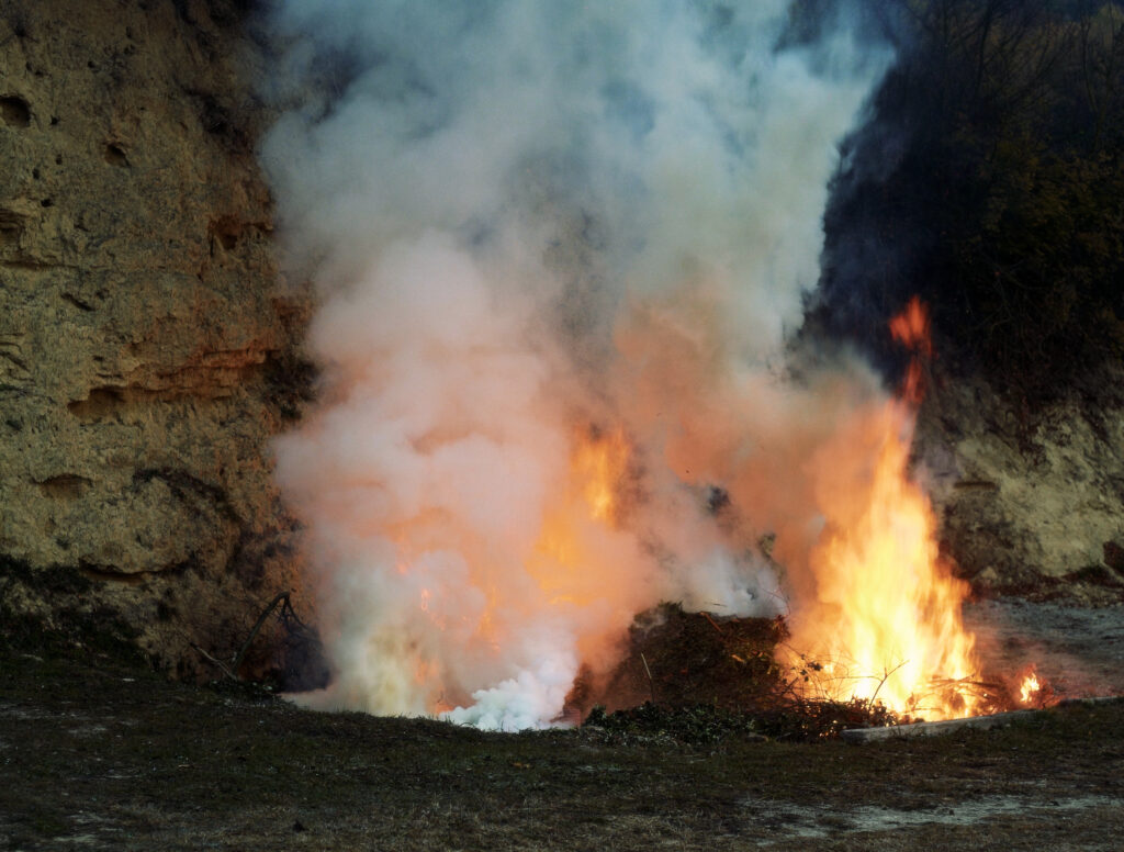 Fum blanc i flames a la pila de restes vegetals del Parc del Castell de Montesquiu, on es cou la peça