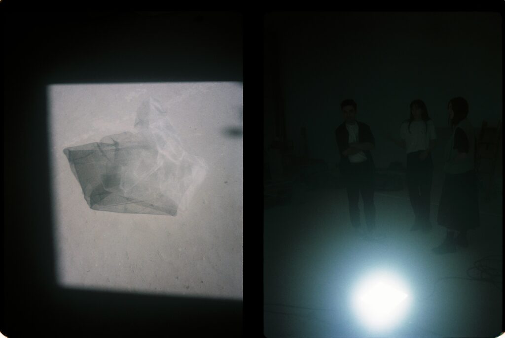Restes de material al terra il·luminades pel sol de la finestra, i tres persones de l'estudi d'arquitectura observant la taula en procés
